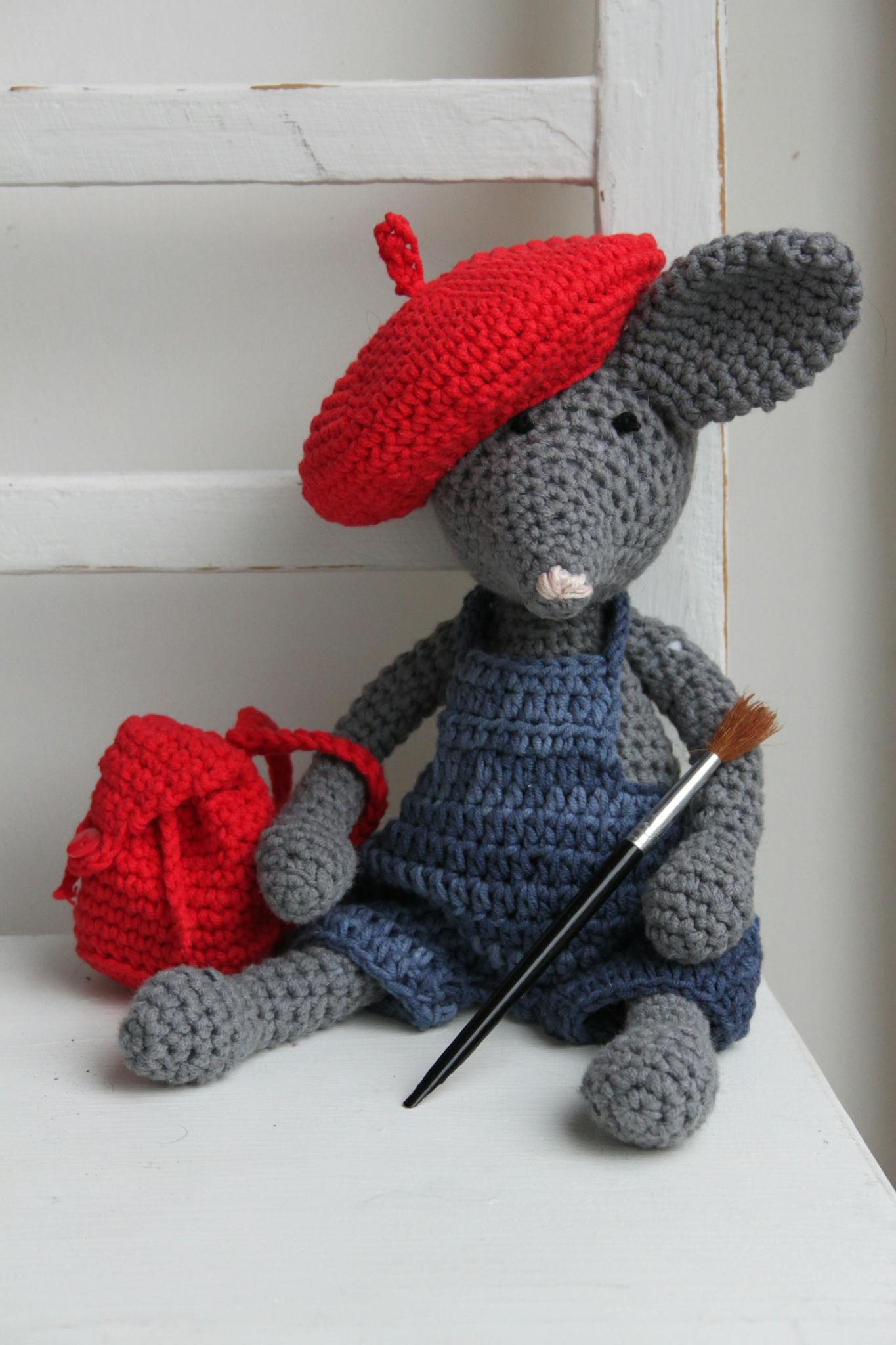 A charming crochet mouse toy dressed as an artist holding a paintbrush, complete with a red beret.